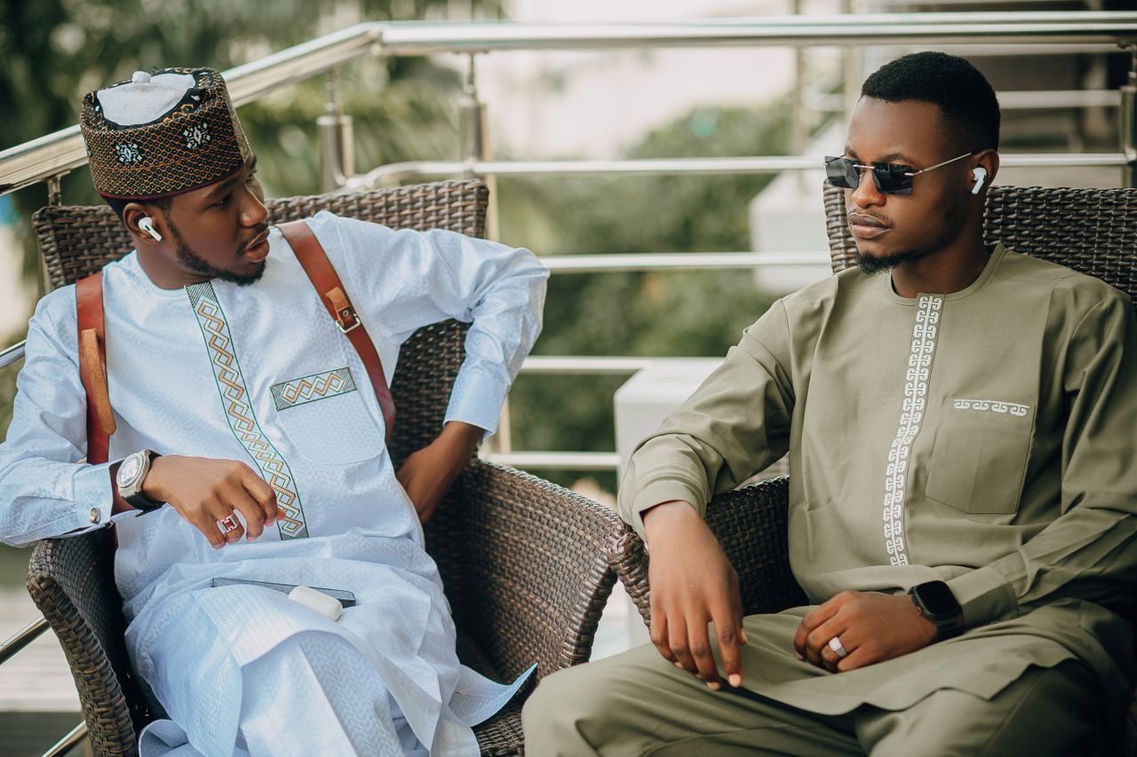 Services-03 Two African men in traditional attire relaxing outdoors, showcasing cultural fashion.
